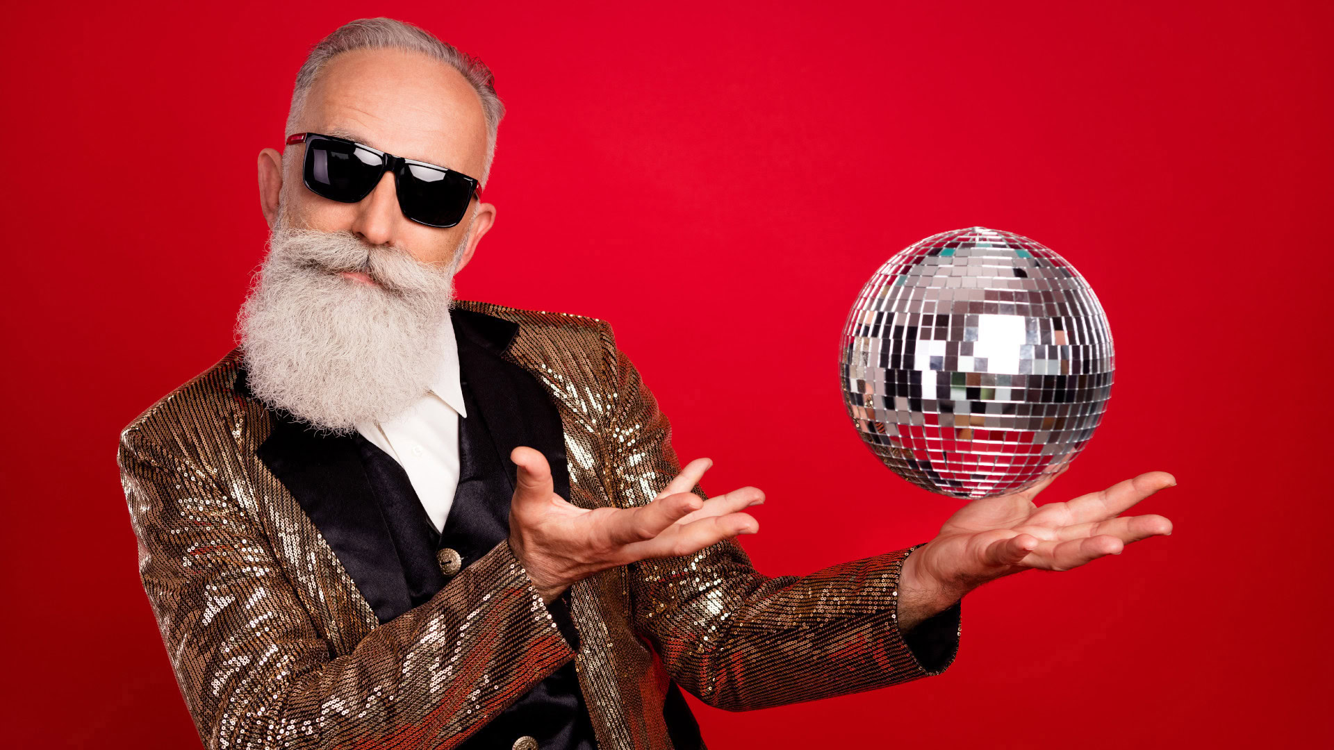 Ein stilvoll gekleideter älterer Mann mit weißem Bart, Sonnenbrille und goldenem Glitzerjackett posiert vor einem knallroten Hintergrund. Er hält eine schwebende Discokugel zwischen seinen Händen. Das Bild symbolisiert, wie Markenvorlieben und persönliche Ausdrucksformen wichtige Hinweise auf die Werte und den Lifestyle einer User Persona geben können.