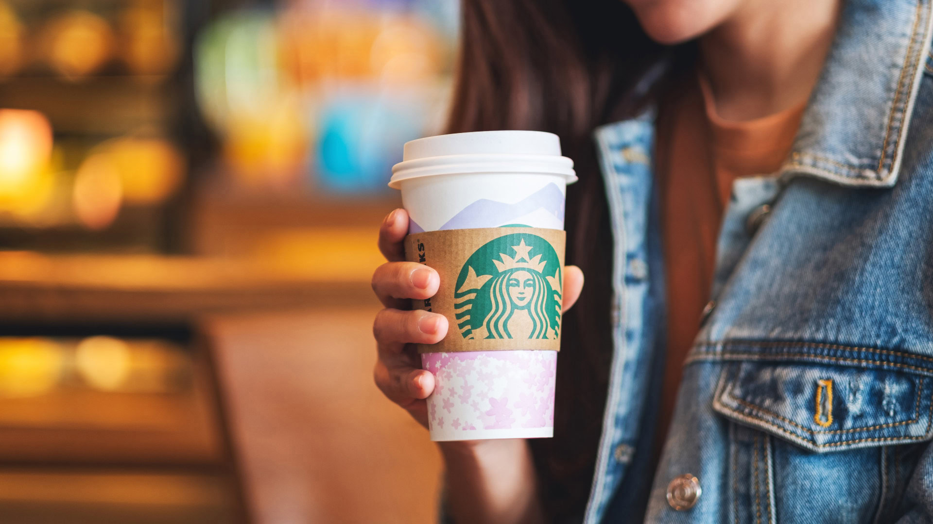 Eine Person hält einen Starbucks-Becher in der Hand, das bekannte grüne Logo ist gut sichtbar. Die Szene spielt sich in einem gemütlichen Café-Ambiente ab, mit warmem Licht und verschwommenem Hintergrund. Starbucks steht als Beispiel für ein innovatives Geschäftsmodell, das durch die Blue-Ocean-Strategie einen neuen Markt geschaffen hat, indem es Kaffee mit einem Erlebnis und einer starken Marke kombiniert.