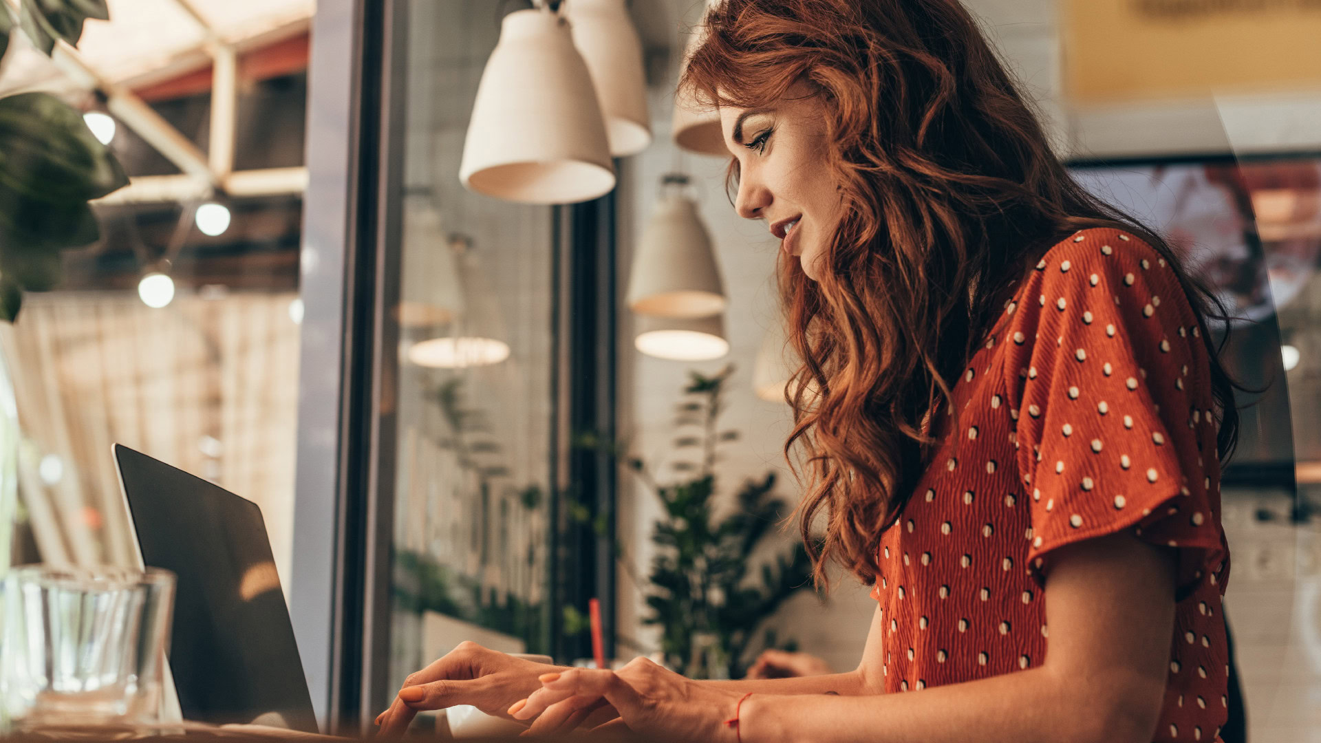 Eine Frau arbeitet konzentriert an ihrem Laptop in einem gemütlichen Café. Diese Szene verdeutlicht die Bedeutung des Kontexts und der Situation innerhalb einer Job Story und zeigt, wie Clarifier zusätzliche wertvolle Informationen liefern können.