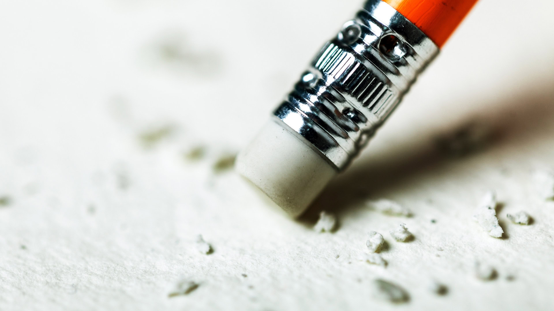 Ein Radiergummi entfernt Schrift auf Papier und hinterlässt kleine Partikel. Veranschaulicht das Entfernen von Metriken und Zahlen aus einem Objective, um den Fokus auf qualitative Zielsetzungen in OKR zu legen.