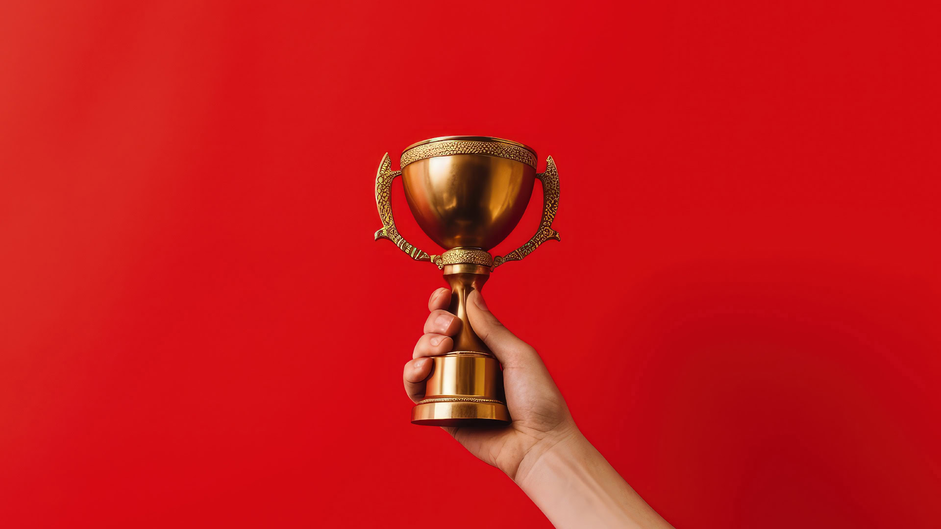 Erfolge zu feiern, fördert ein Growth Mindset. Das Bild zeigt eine Hand, die einen goldenen Pokal vor einem roten Hintergrund hält – ein Symbol für erreichte Ziele und persönliches Wachstum.
