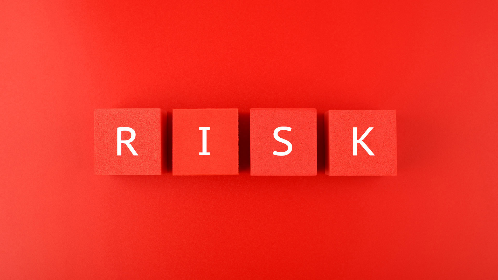 Vier rote Würfel vor einem roten Hintergrund, die das Wort RISK bilden.