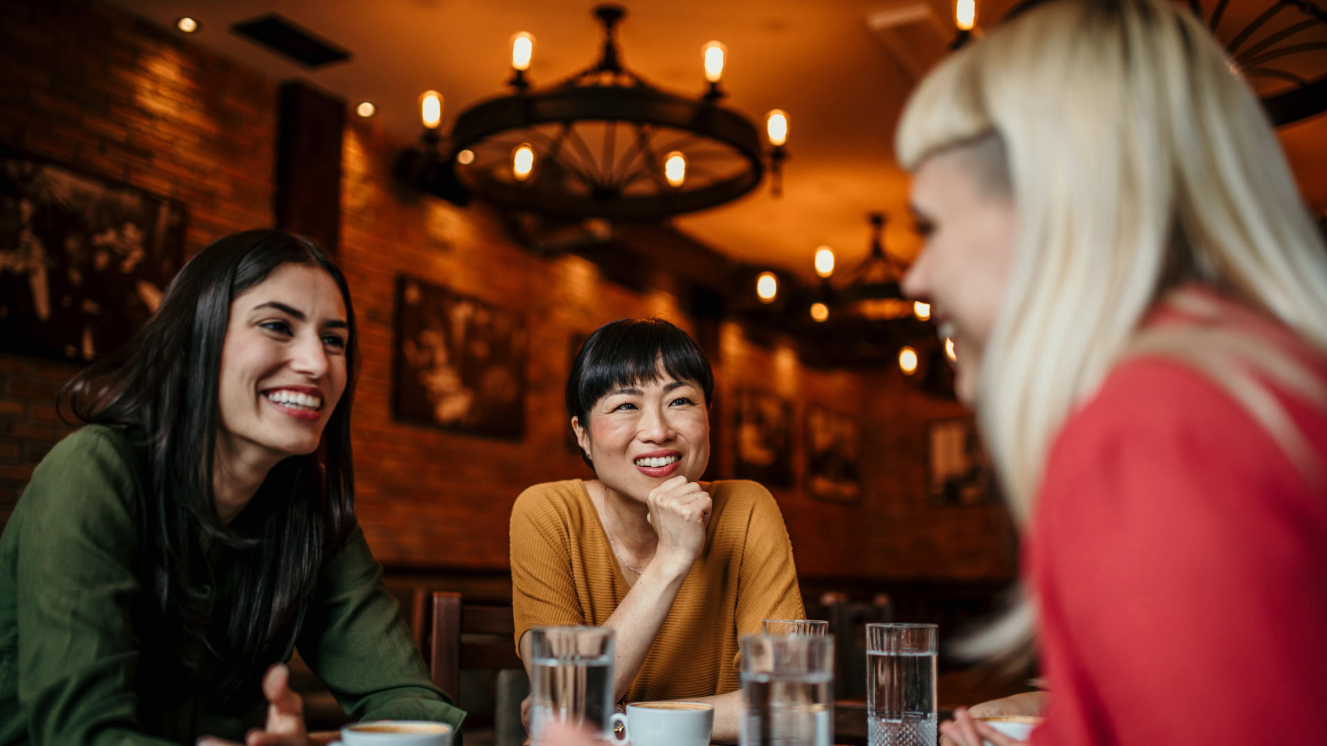 Zwei aufmerksame Zuhörerinnen sitzen mit einer Gesprächspartnerin in entspannter Atmosphäre in einem Café, während sie ein User Interview durchführen.