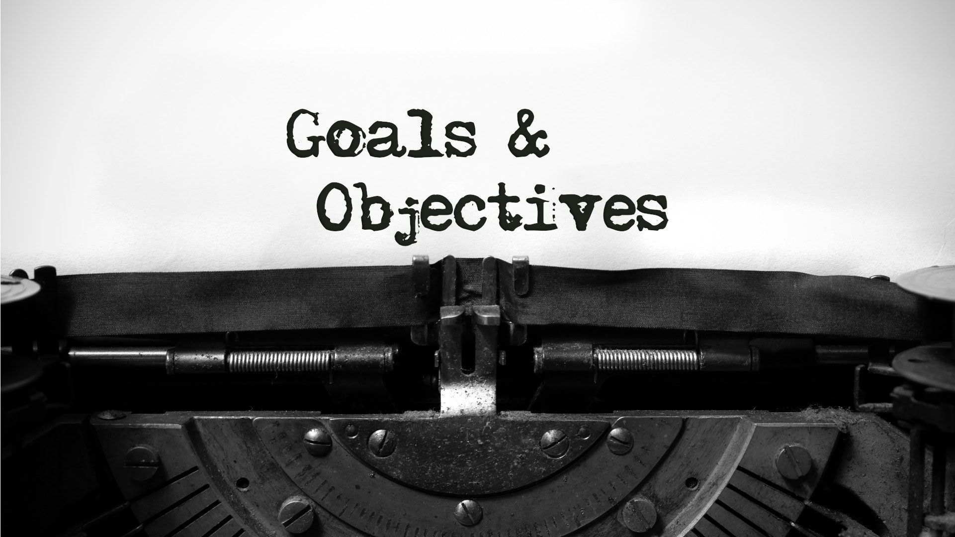 Alte Schreibmaschine mit eingespanntem Papier, auf dem in grober Schrift "Goals & Objectives" getippt wurde, verdeutlicht die Unterscheidung zwischen Zielen und Objectives in der strategischen Planung.