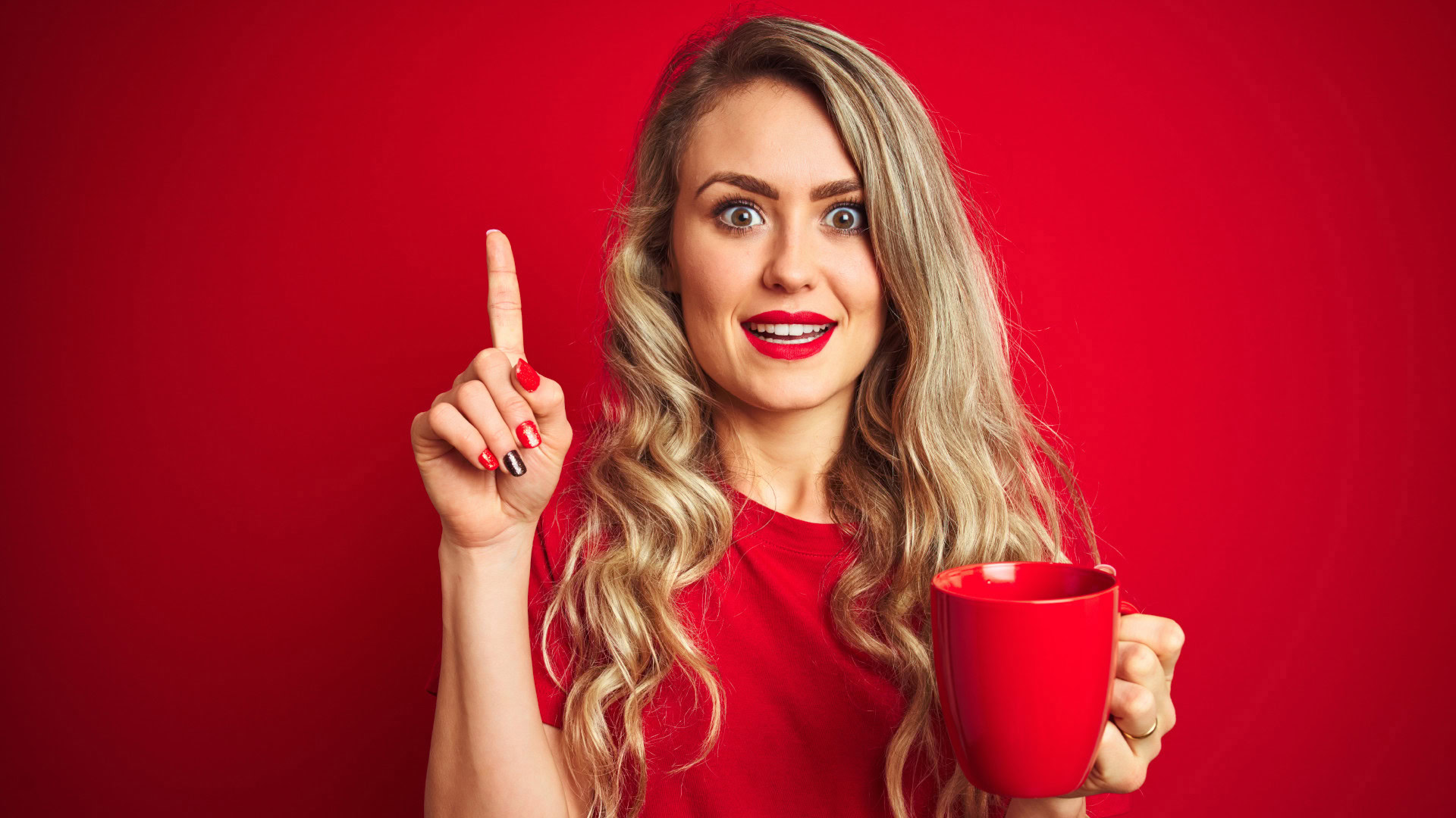 Frau mit rotem Shirt und passender Tasse hebt mahnend den Finger und erinnert daran, sich in User Interviews nicht von den Ideen der Nutzer vorschnell leiten zu lassen.