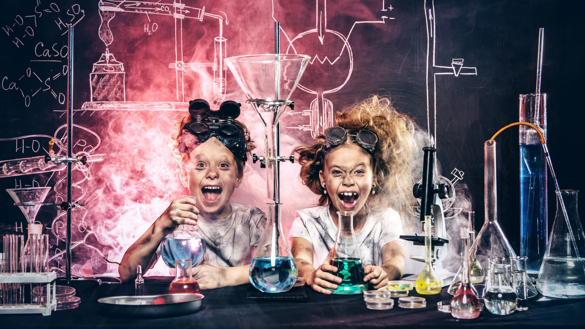 Zwei Kinder in verschmutzten Laborkitteln mit aufgeregten Gesichtern führen ein verrücktes Experiment durch, umgeben von Kreidezeichnungen und Rauch.