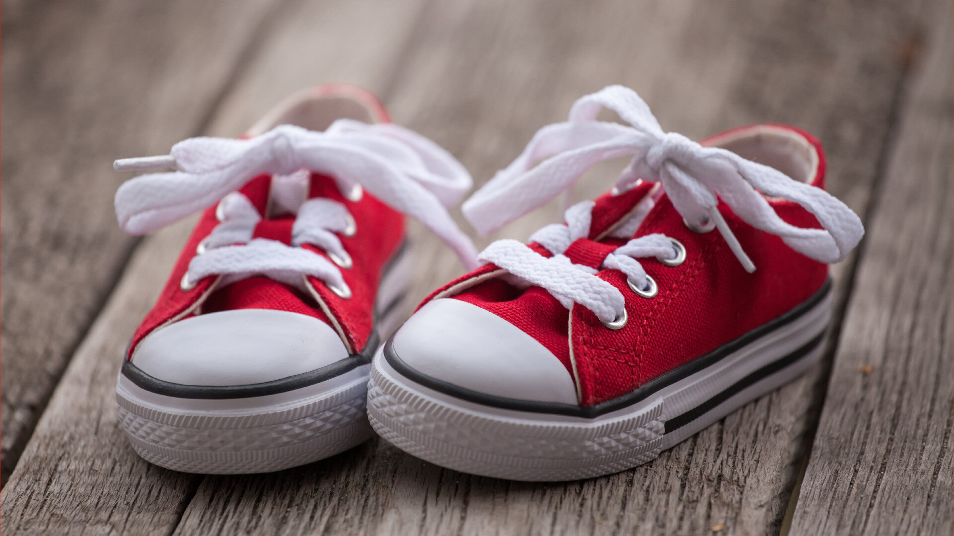 Zwei kleine rote Sneaker auf einem Holzsteg.