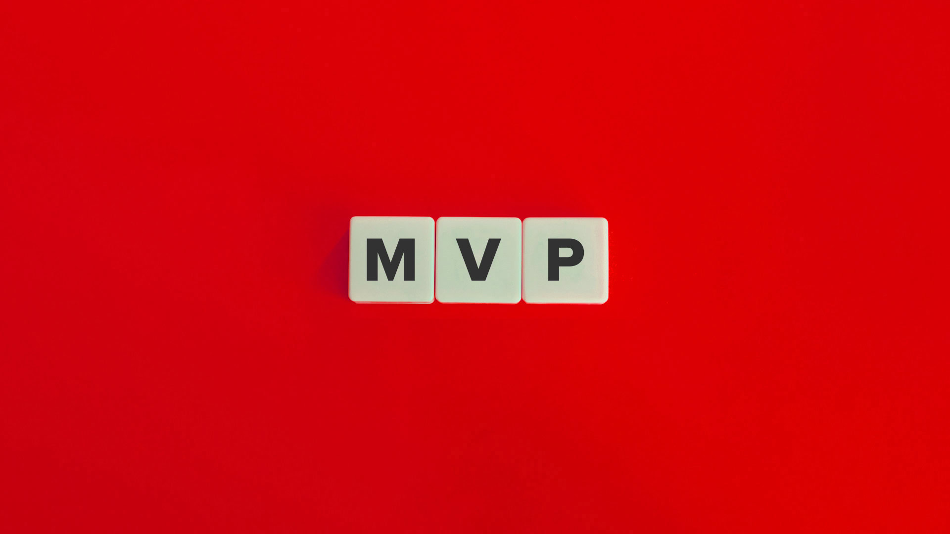 Drei weiße Spielsteinbuchstaben mit der Aufschrift MVP auf einem roten Hintergrund, die für Minimum Viable Product stehen.