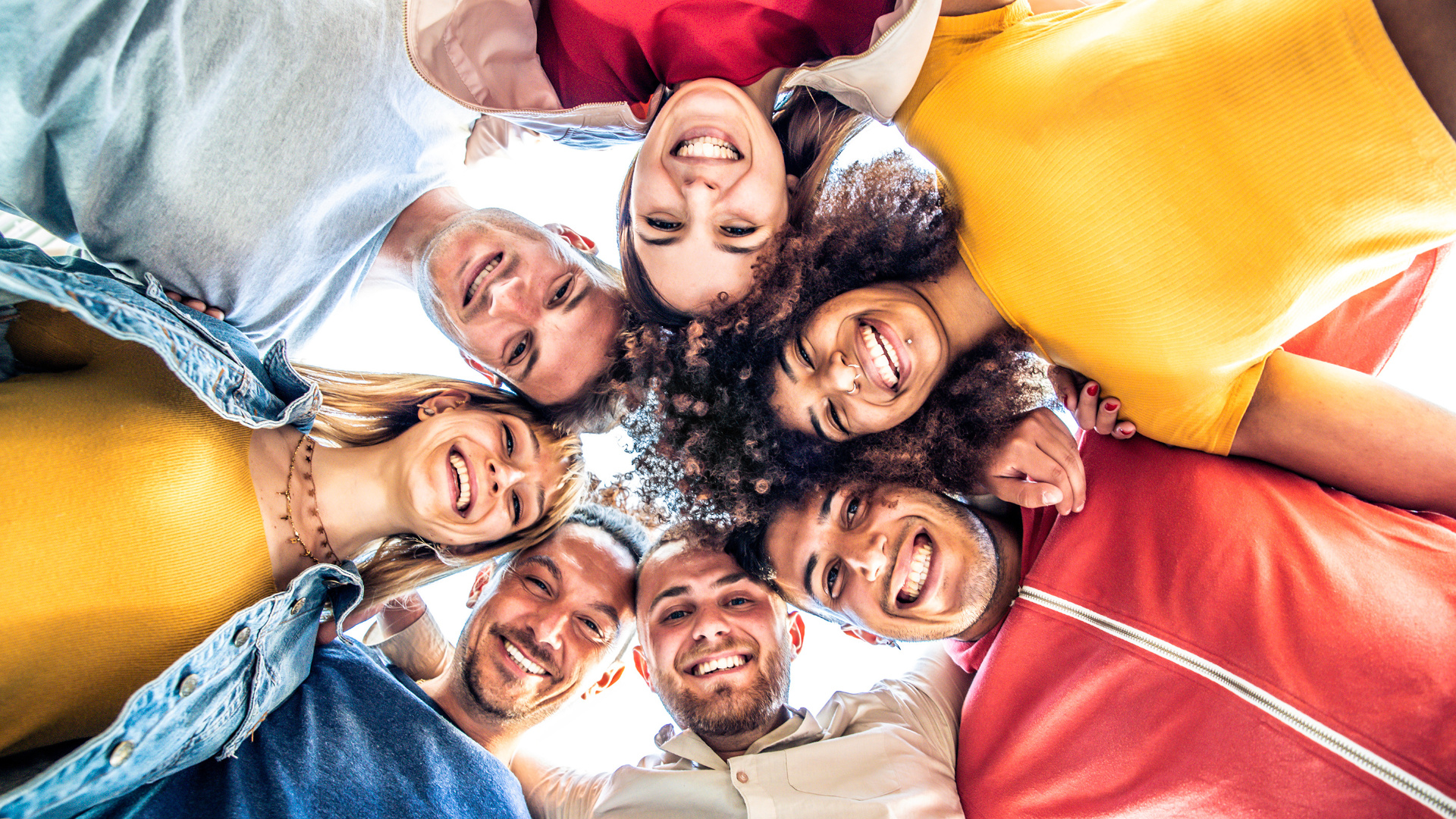 OKR Circle: Eine Gruppe junger Menschen steht im Kreis, Arm in Arm, lächelt in die Kamera und symbolisiert Teamgeist und Zusammenarbeit.