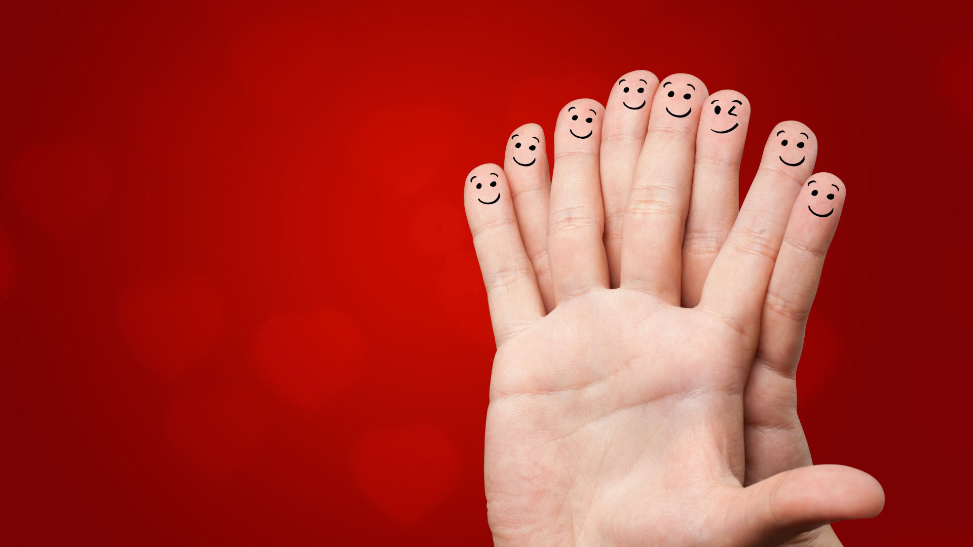 Eine Mastermind-Gruppe lebt von der Vielfalt und dem engen Austausch ihrer Mitglieder. Das Bild zeigt zwei ineinander verschränkte Hände mit aufgemalten Smileys auf den Fingerspitzen vor einem roten Hintergrund. Die lachenden Gesichter symbolisieren die enge Verbindung, das Vertrauen und den unterstützenden Charakter einer Mastermind-Gruppe.