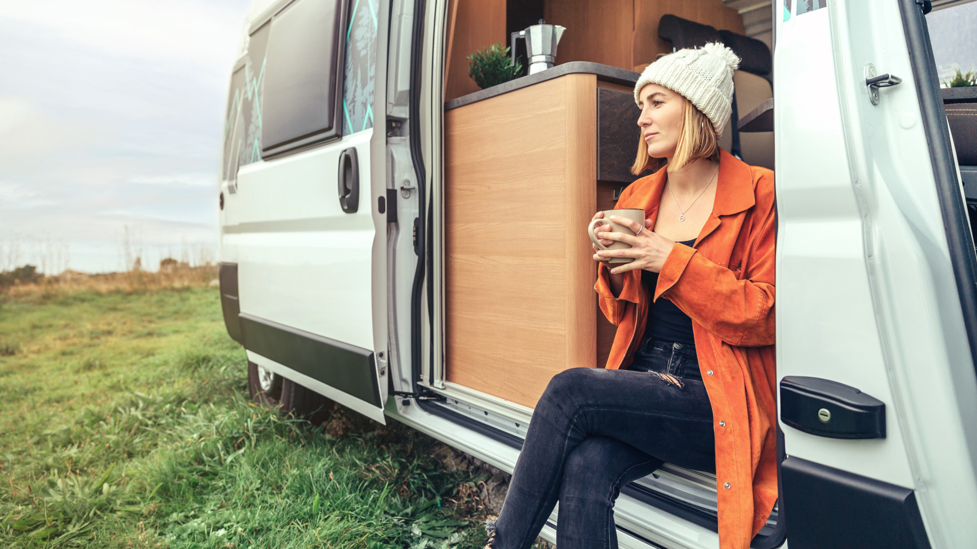 Reisebloggerin Nora sitzt mit Kaffeetasse im Campervan und genießt die Landschaft
