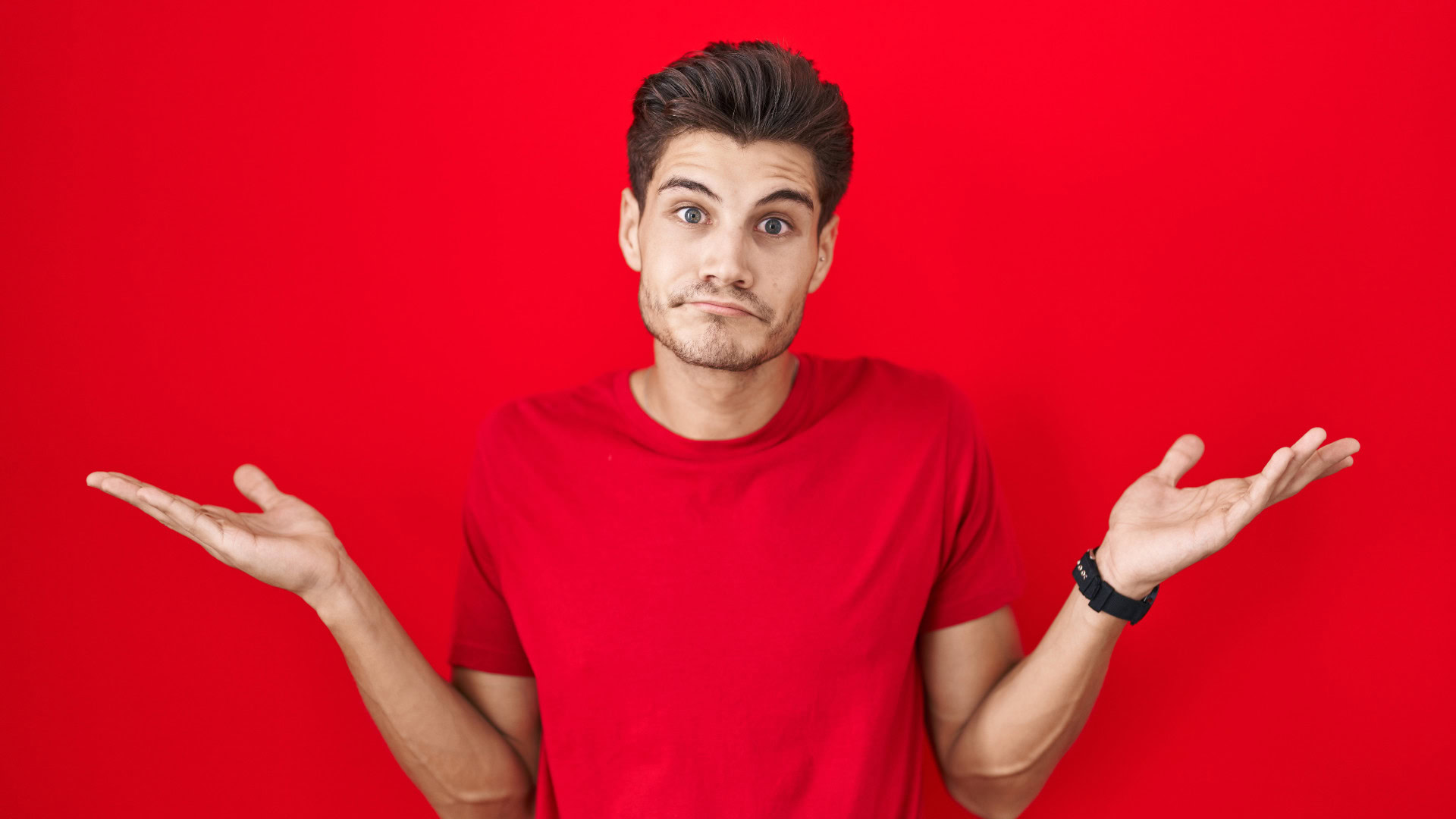 Ein junger Mann in einem roten T-Shirt steht vor einem roten Hintergrund und zuckt mit den Schultern, während er verwirrt schaut. Das Bild symbolisiert die Unsicherheit oder Verwirrung, die beim Festlegen von SMART Zielen entstehen kann.