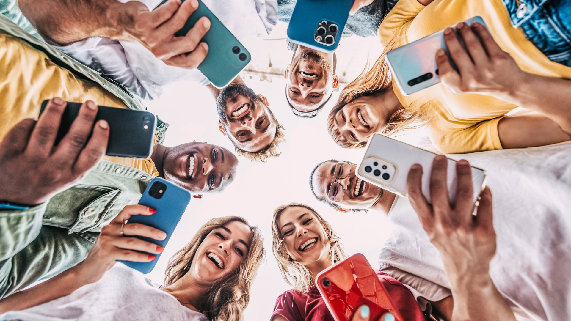 Eine Gruppe junger Menschen hält lachend ihre Smartphones in die Kamera – ein Symbol für Early Adopter, die neue Technologien und Trends auf Social Media entdecken, teilen und verbreiten.