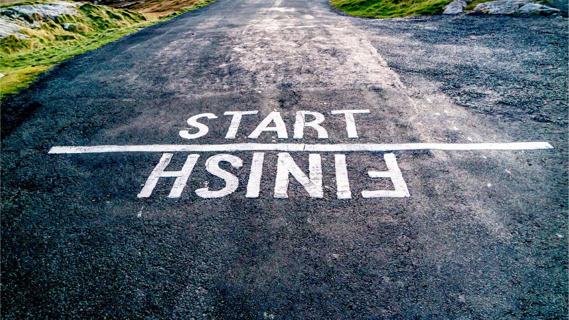 Die Worte Start und Finish sind auf eine asphaltierte Straße gemalt, wobei Finish auf dem Kopf steht. Dies veranschaulicht die Bedeutung von Start- und Zielwerten für Key Results in OKR, um Fortschritte klar messbar zu machen.