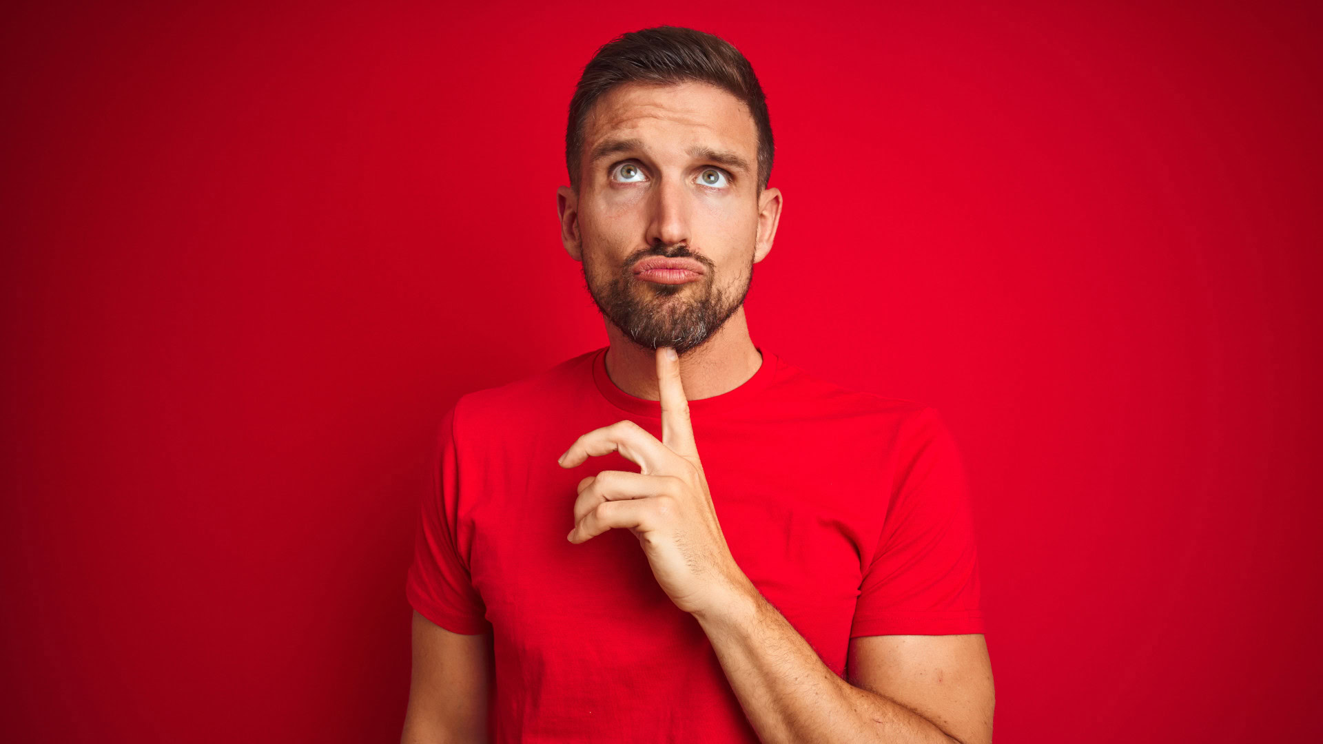Ein nachdenklicher Mann in rotem Shirt berührt sein Kinn, was den Moment des ersten Gedankens symbolisiert, der oft der Auslöser für eine Kaufentscheidung in einem Switch Interview ist.