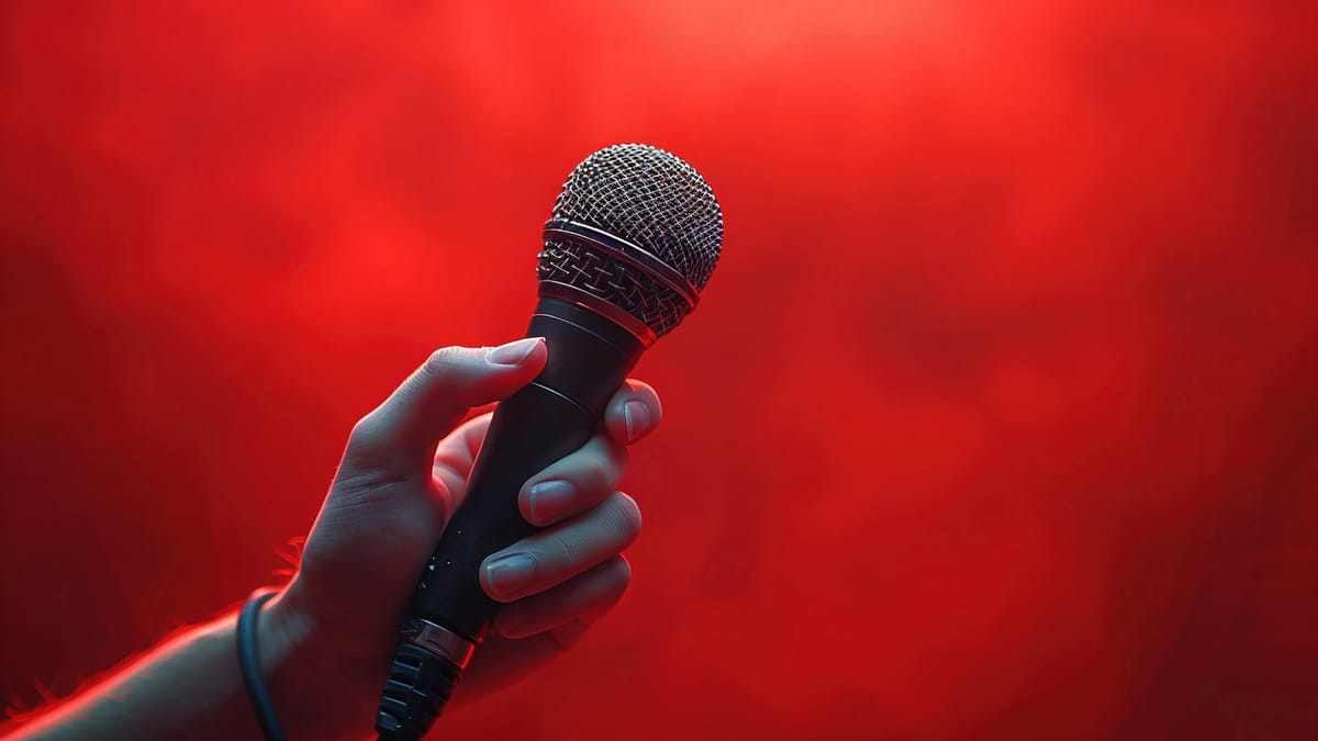 Eine Nahaufnahme einer Hand, die ein Mikrofon hält, vor einem leuchtend roten, unscharfen Hintergrund. Das Bild symbolisiert