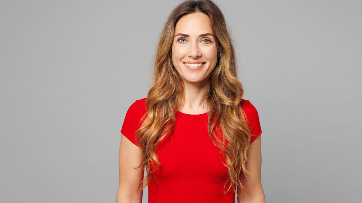 Porträt einer lächelnden Frau mit langen, welligen Haaren in einem roten Shirt vor neutralem grauem Hintergrund als Beispiel
