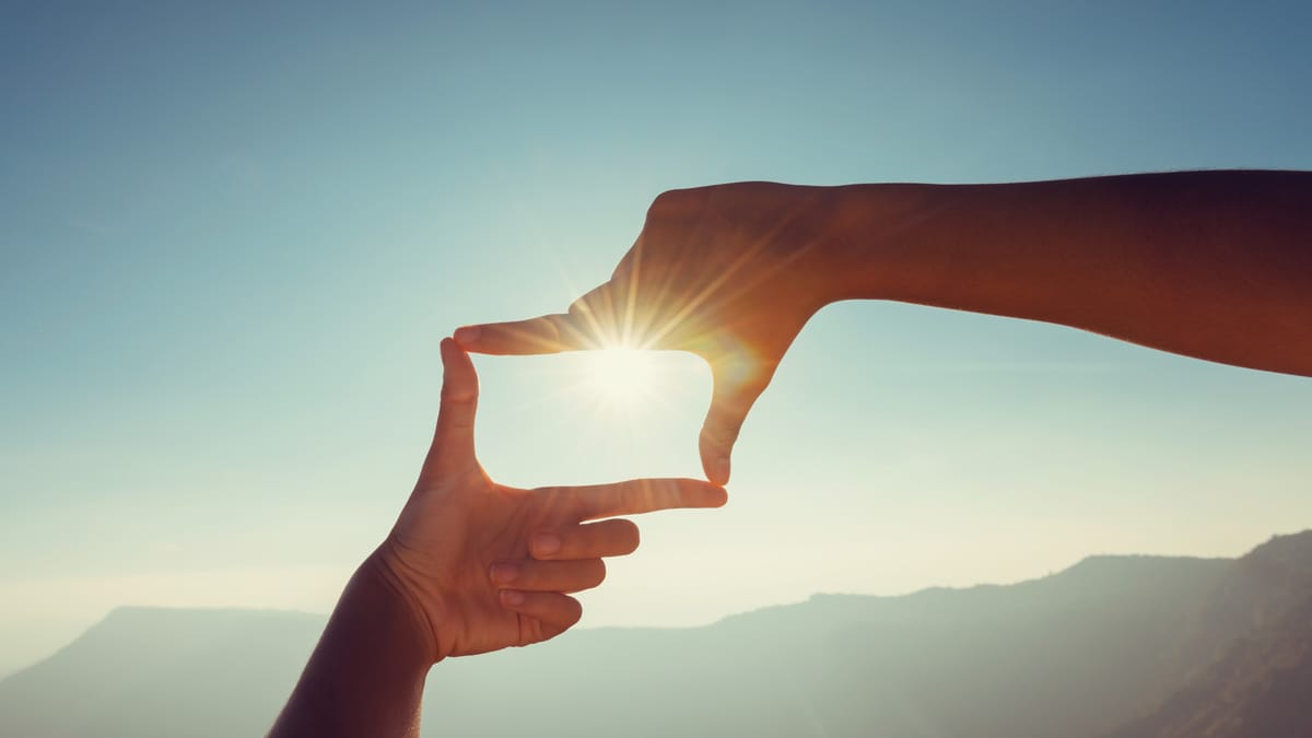 Zwei Hände formen mit Daumen und Zeigefinger einen viereckigen Rahmen, durch den die Sonne scheint.