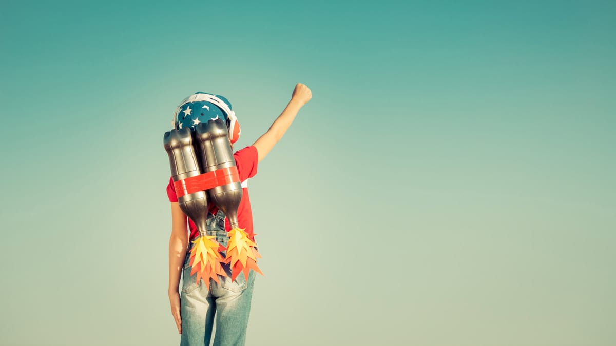 Ein Kind mit einem selbstgebauten Raketenrucksack aus Flaschen und Papierflammen steht mit erhobenem Arm vor einem klaren Him