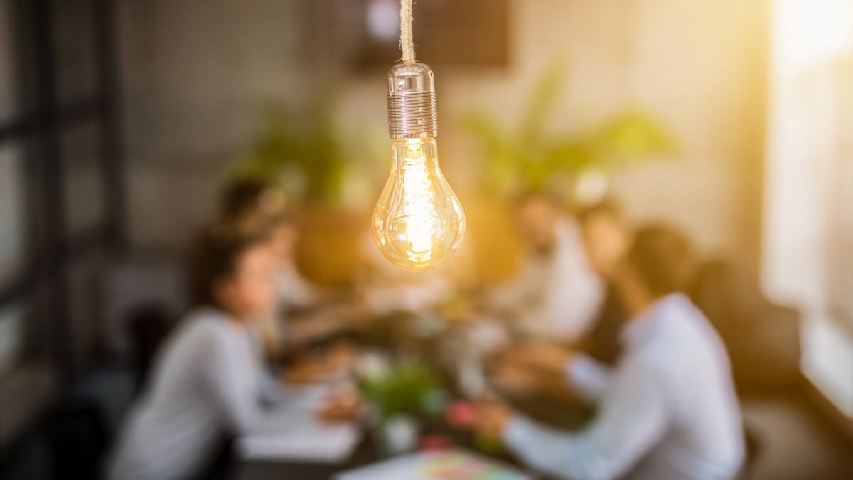 Leuchtende Glühbirne als Symbol für Ideenfindung — im Hintergrund unscharf eine Gruppe von Menschen in Diskussion bei einem B