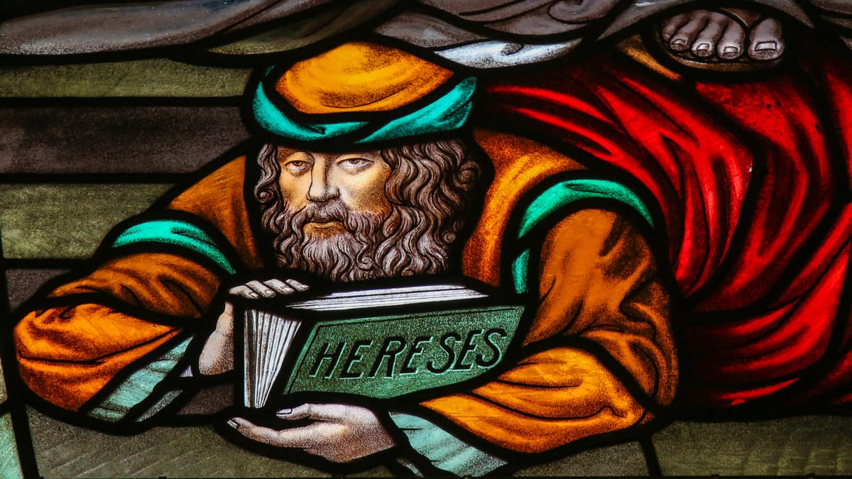 Ein buntes Kirchenfenster zeigt einen bärtigen Mann in orange-grüner Kleidung, der ein Buch mit der Aufschrift HERESES in den Händen hält. Er wird vom Fuß eines anderen zu Boden gedrückt.