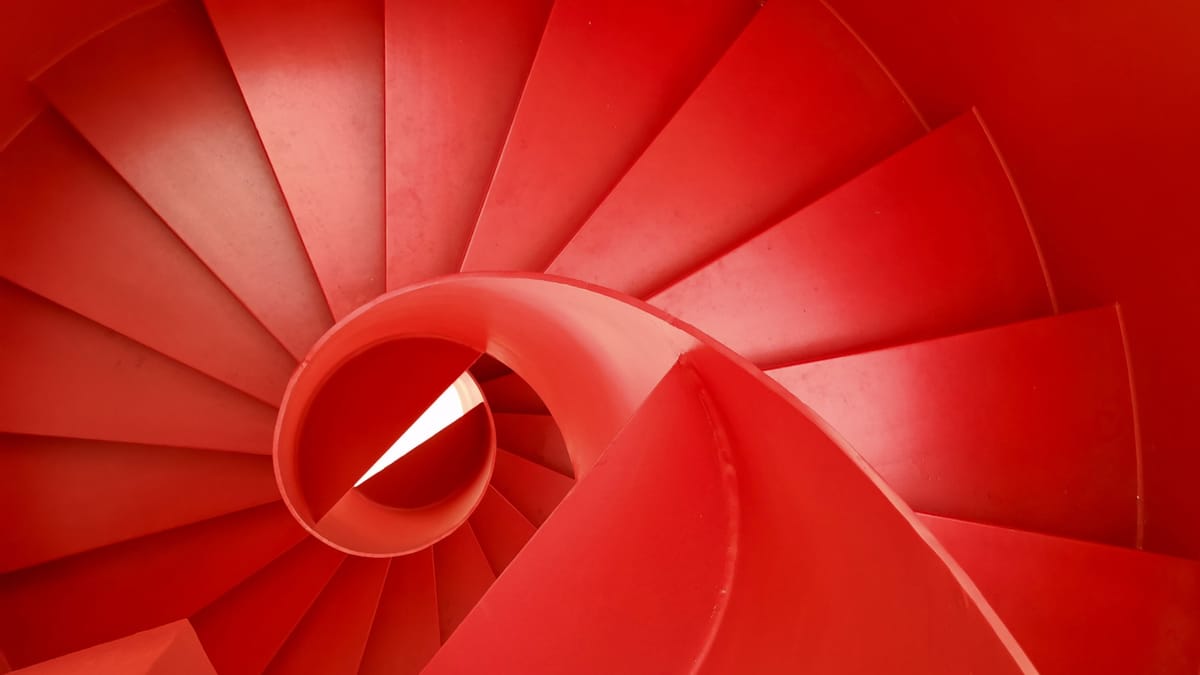 Rote Wendeltreppe in spiralförmiger Perspektive von oben fotografiert, mit starkem geometrischem und grafischem Effekt.