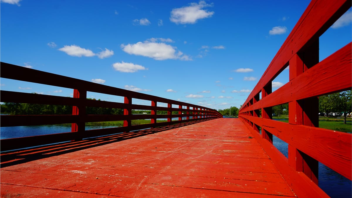 Rote Holzbrücke über einem Fluss unter strahlend blauem Himmel mit weißen Wolken.