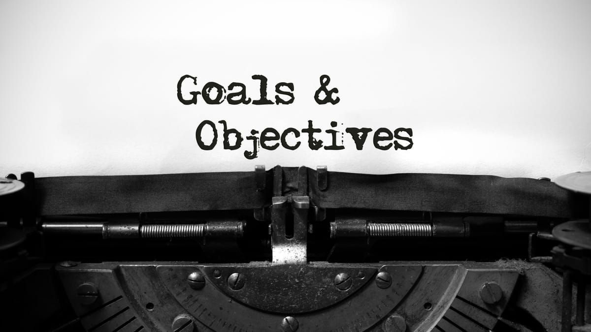 Schreibmaschine, in die ein Blatt Papier eingespannt ist. Auf dem Blatt steht in "Goals & Objectives".