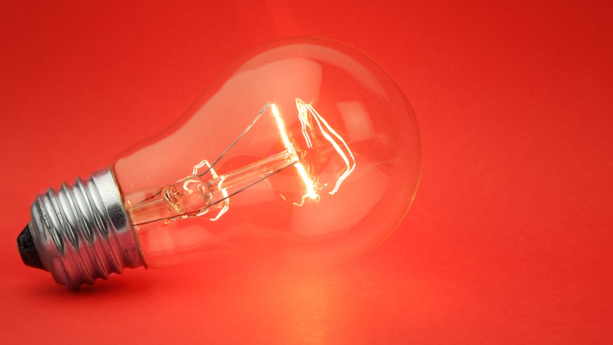 Eine leuchtende Glühbirne liegt auf einem roten Untergrund.