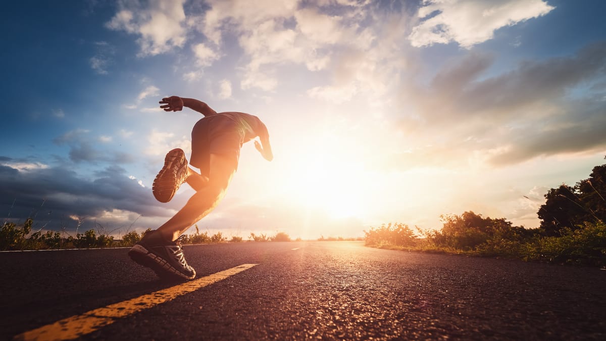 Ein Läufer sprintet auf einer Straße in Richtung Sonnenaufgang.