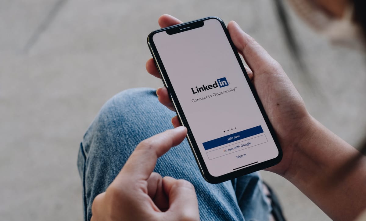Solopreneur hält ein Handy in der Hand, auf dessen Display der Login-Screen von LinkedIn zu sehen ist.