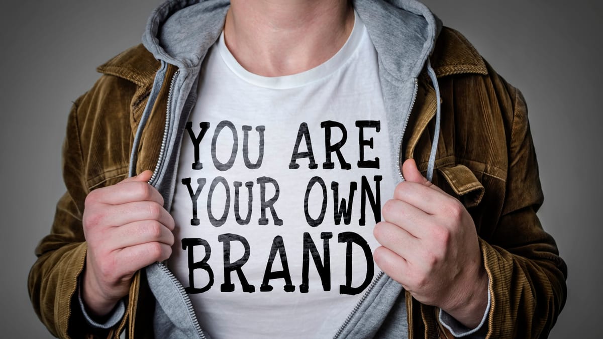 Solopreneur in brauner Jacke reißt sein Hoodie auf und zeigt ein weißes T-Shirt mit dem Aufdruck "You Are Your Own Brand"”.